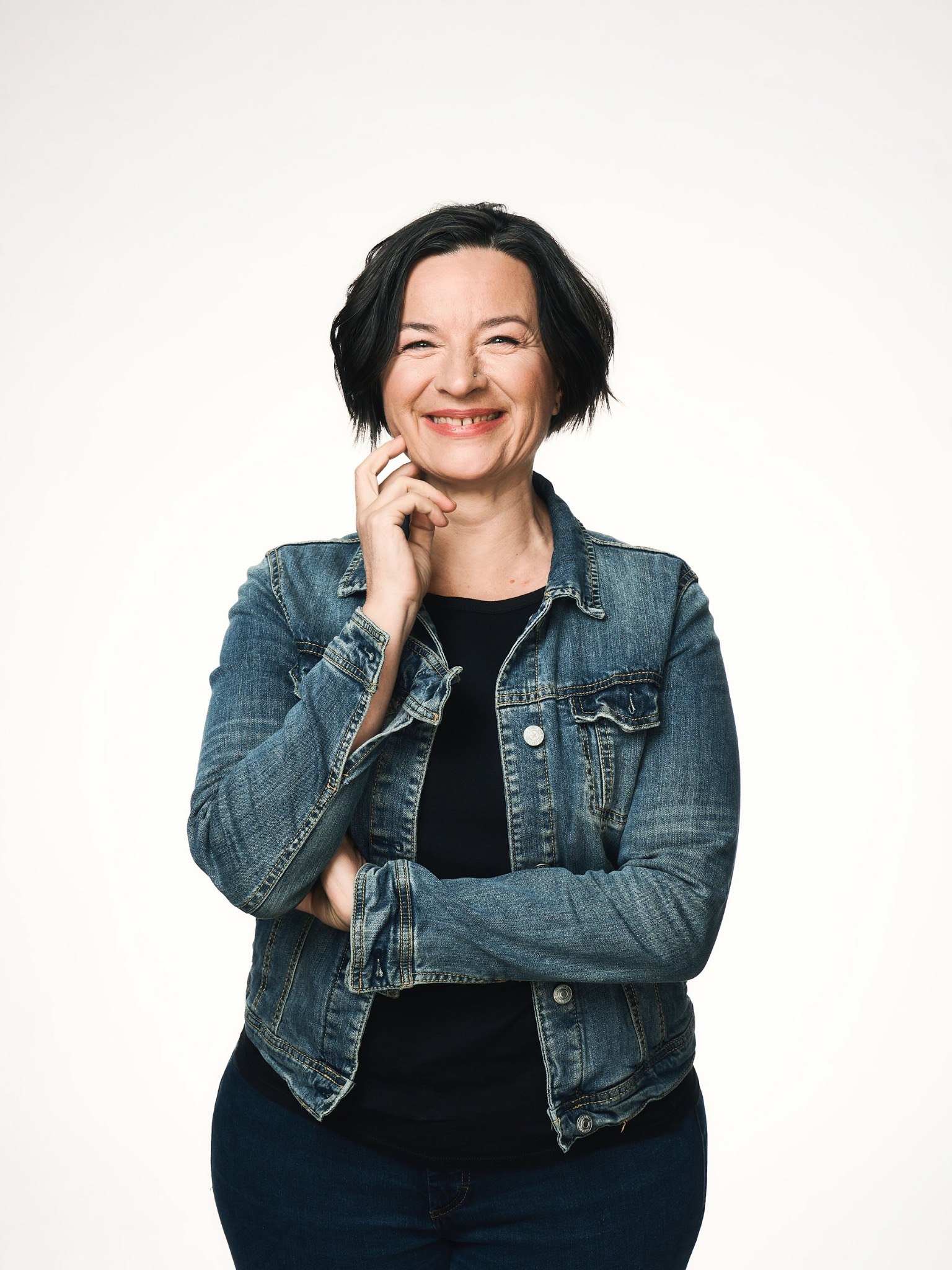 Brenda Stys lächelt vor hellem Hintergrund in einer Jeansjacke